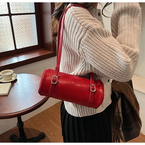 Detail of red cylindrical shoulder bag with adjustable straps on model in cafe