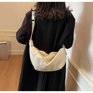 Detailed back view of a beige minimalist crescent bag worn over a black coat