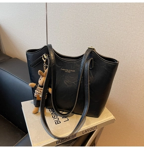 Close-up of black leather tote bag with gold lettering and a cute bear charm accessory