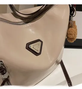 Close-up of glossy cream leather shoulder bag featuring triangular metal logo and brown trim