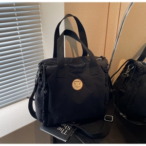 Close-up of black canvas tote bag with fashion bear patch and woven handles detail