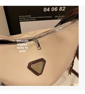 Detailed close-up of smooth metal zipper and minimalist triangular plaque on beige bag