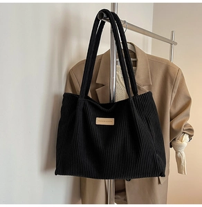 Detail of black corduroy tote bag showing ribbed texture and brown leather label