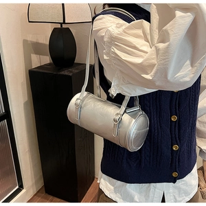Detailed view of a metallic silver barrel shoulder bag worn by a model in a modern room