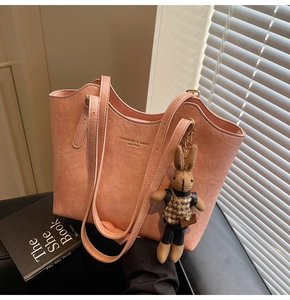 Detail of light pink faux leather tote bag with gold logo and plush rabbit pendant