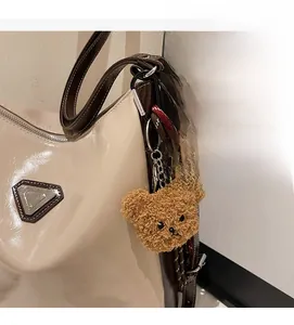 Close-up of a brown teddy bear plush charm attached to a cream faux leather tote bag