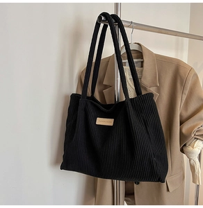 Detail of black corduroy tote bag featuring a leather fashion label and soft texture