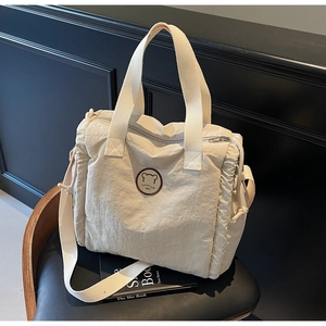 Detail of off-white canvas tote bag with bear patch on a black leather chair