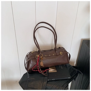 Détail d'un sac baguette vintage marron foncé avec œillets métalliques et porte-clés décoratif