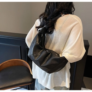 Detail of a black pleated leather shoulder bag showing the drape and wide strap