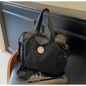 Detail of black nylon tote bag featuring round bear logo patch and adjustable strap