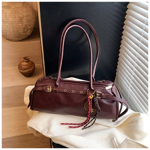 Détail du sac baguette en cuir bordeaux avec œillets métalliques et breloque déco