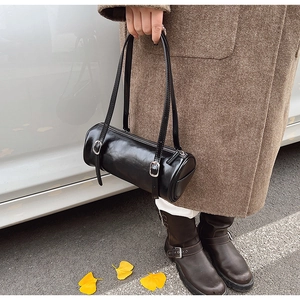 Detailed macro view of black glossy cylinder shoulder bag with silver metal buckles