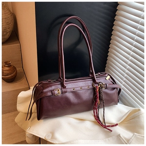 Vue détaillée du sac cylindre bordeaux avec boucles dorées sur une veste beige