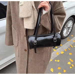 Detailed close-up of glossy black barrel shoulder bag with silver buckle straps in autumn