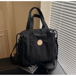 Close-up of black canvas tote bag with brown bear logo patch on dark leather seat