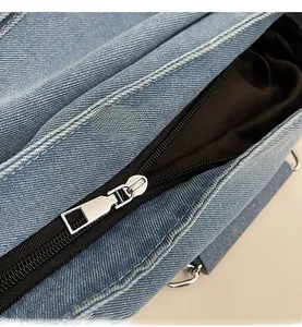 Detail of silver smooth metal zipper and white stitching on light blue denim tote bag