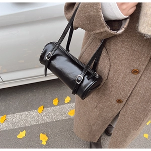 Chic black barrel shoulder bag with double buckles worn by model in autumn scenery