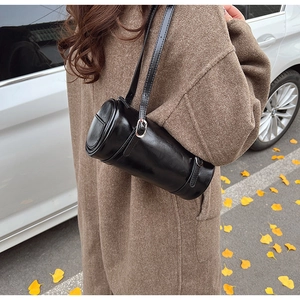 Close-up of black cylinder shoulder bag in glossy leather with silver metal buckles