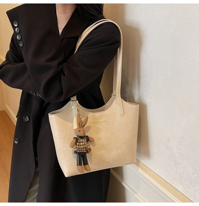 Detail view of cream tote bag with leather texture and cute rabbit charm on a model