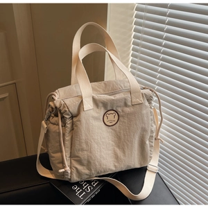 Detail of beige tote bag featuring crinkled texture, bear patch, and adjustable shoulder strap