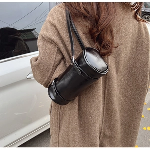 Detail view of a minimalist black cylindrical shoulder bag with polished PU leather finish