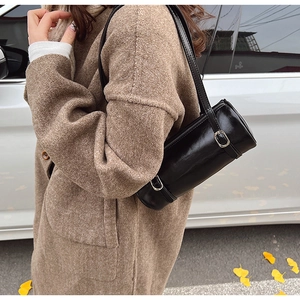 Close-up of a black cylinder shoulder bag with silver buckle on a stylish model