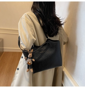 Detail of black pebbled leather tote bag with gold logo and plush rabbit charm
