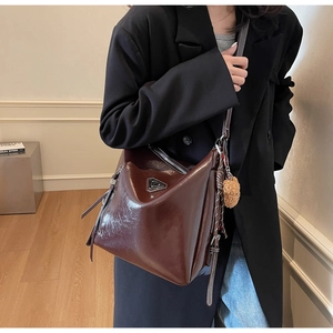 Detail of dark brown leather bucket bag with metal logo and plush keychain