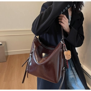 Detail of dark brown glossy hobo bag with metal buckle and cute plush bear charm
