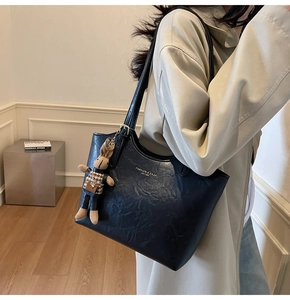 Detail of a black leather tote bag with a rabbit charm on a model in a beige coat