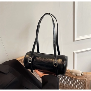 Detail of black cylindrical shoulder bag featuring glossy leather texture and silver buckles