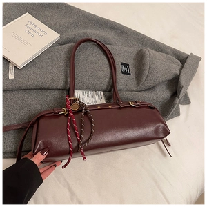 Détail du sac baguette en cuir bordeaux avec breloque cordelette sur fond de laine