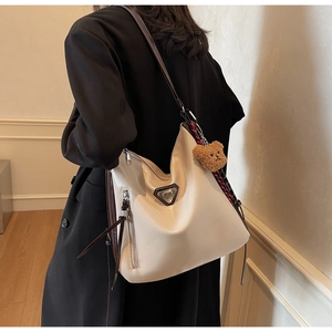 Detail of a creamy white glossy hobo bag with brown leather strap and plush bear charm