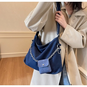 Detail view of large denim tote bag featuring silver chain decor and small hanging purse