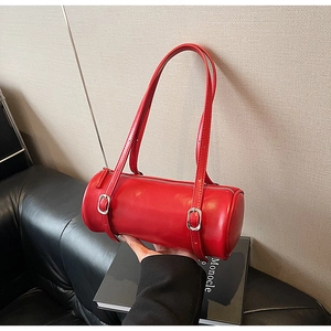 Detail of red cylindrical shoulder bag featuring glossy texture and silver metal buckle