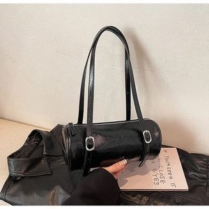 Close-up of a glossy black cylinder shoulder bag featuring silver buckle adjustments