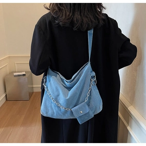 Blue denim tote bag with silver chain strap and small matching pouch shown on shoulder