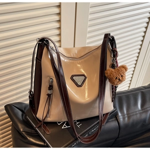 Detail of a beige and coffee crossbody bag with metallic triangle and plush bear charm