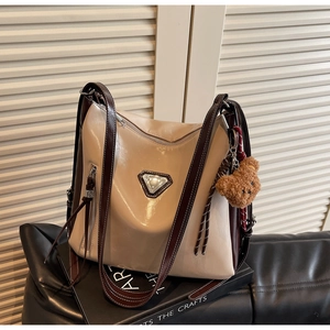 Detail view of beige and brown crossbody bag with decorative bear charm on books