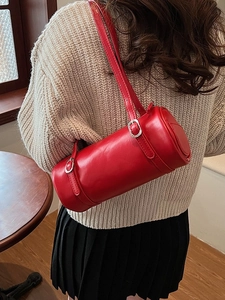 Minimalist red cylindrical shoulder bag in faux leather worn by a model in a warm room