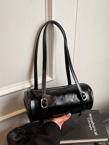 Minimalist black cylinder shoulder bag in glossy leather with adjustable double straps