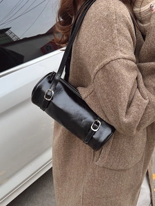 Minimalist black cylinder shoulder bag in glossy leather shown on a model outdoors
