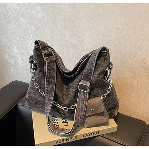 Detail view of large denim tote bag with silver chain and mini pouch on leather sofa