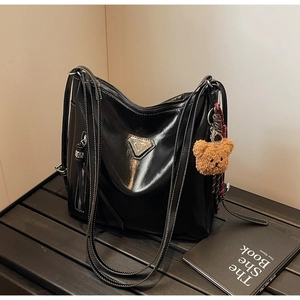 Detail of glossy black leather bucket bag with white stitching and plush bear charm