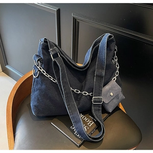 Detail of dark blue denim hobo bag with silver chain on a black leather chair