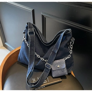 Detail of dark blue denim tote bag with silver chain and mini pouch on wooden chair