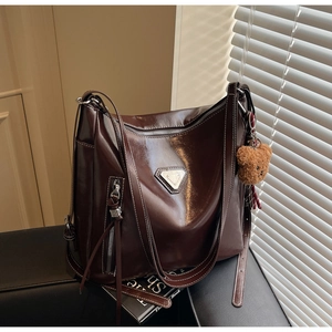Detail of a dark brown glossy leather tote bag with a small bear charm and metal emblem