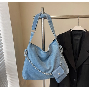 Detail of light blue denim tote bag featuring decorative silver chain and small pouch