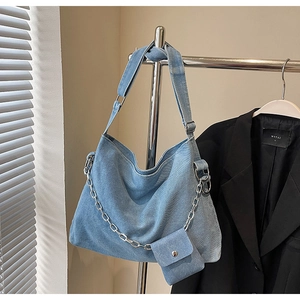 Macro detail of blue denim hobo bag featuring silver chain and mini pouch charm
